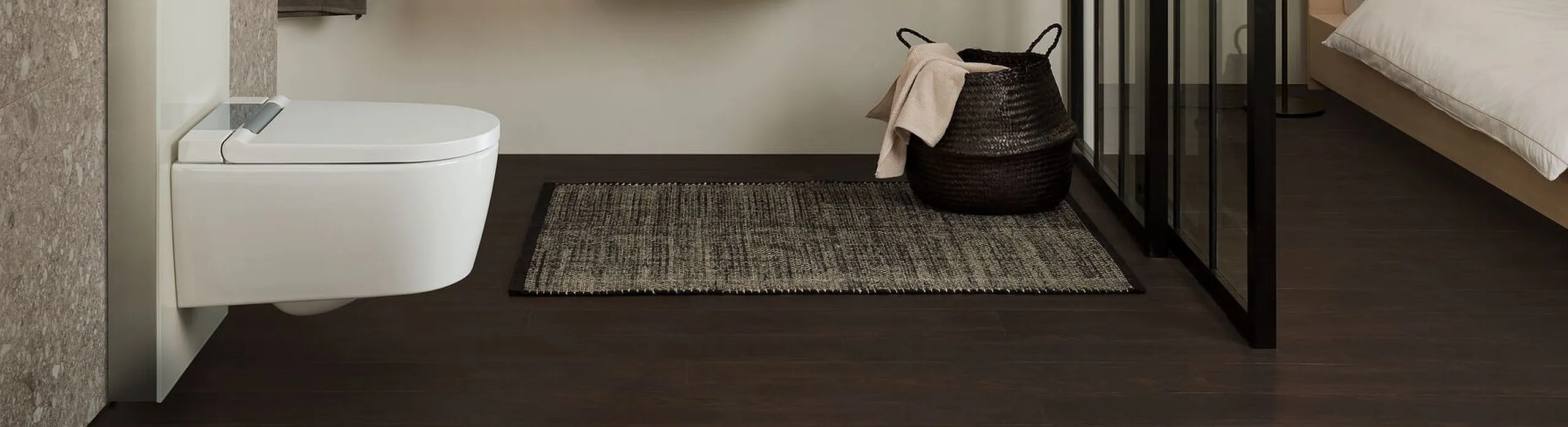 Wohnliches Bad mit wandhängendem Dusch-WC, Holzwaschtisch, Glasabtrennung und schwarzem Korb. Schlichte, moderne Gestaltung.