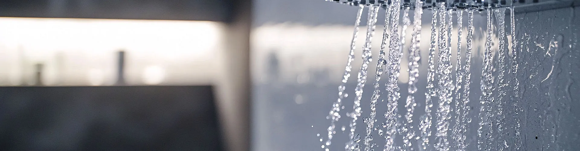 Ein minimalistischer Duschkopf in modernem Design lässt kaskadierende Wasserstrahlen in feinem Muster fließen.