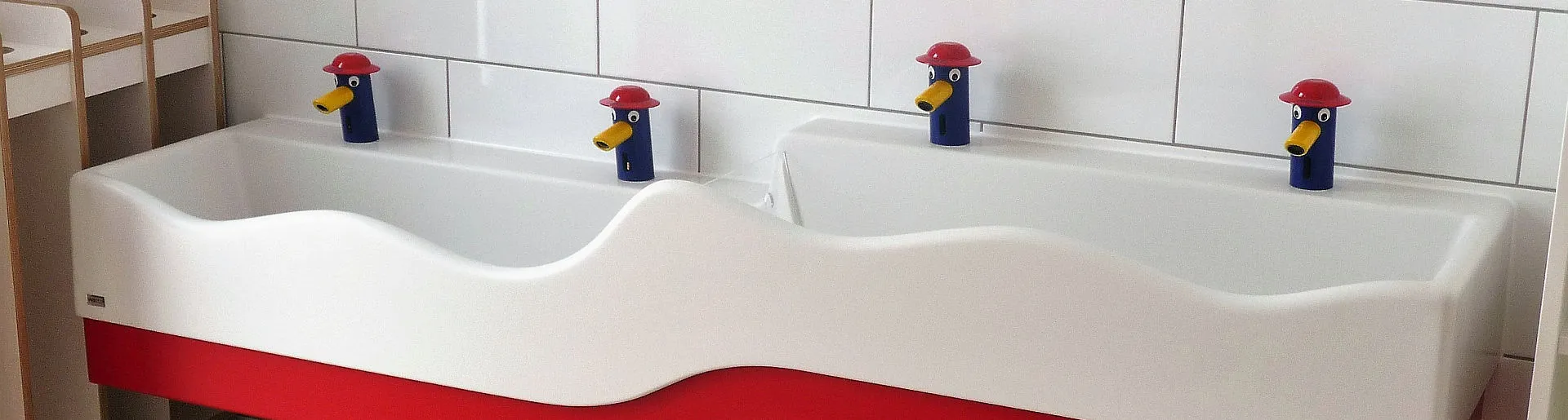 Wandmontierte Dopplewaschtisch mit Feuerwehrarmaturen in einer Kita.