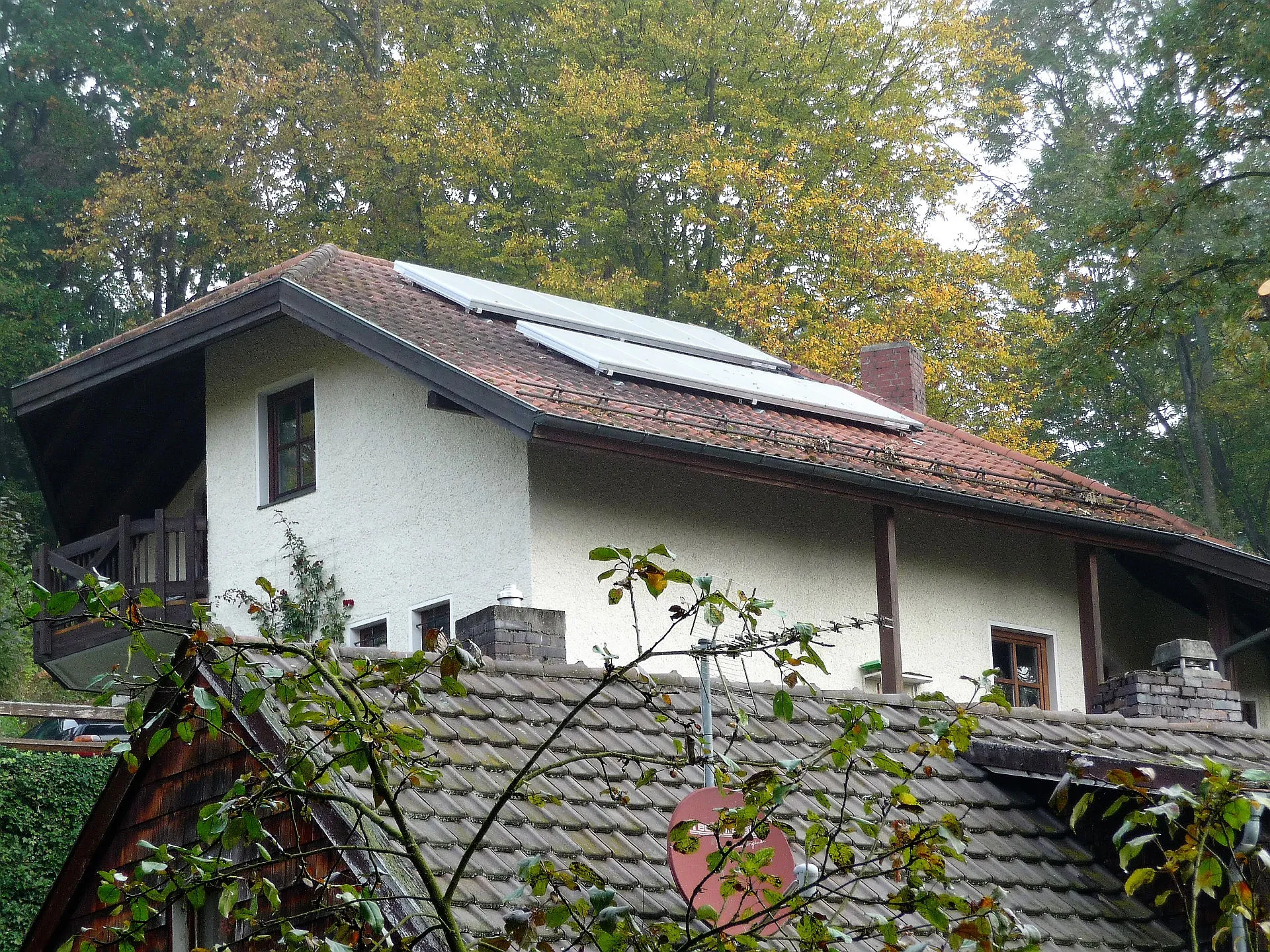 Alt-Text Vorschlag 1: Ein Einfamilienhaus mit rotem Ziegeldach ist mit einer thermischen Solaranlage ausgestattet, die auf der sonnenzugewandten Dachseite installiert ist.