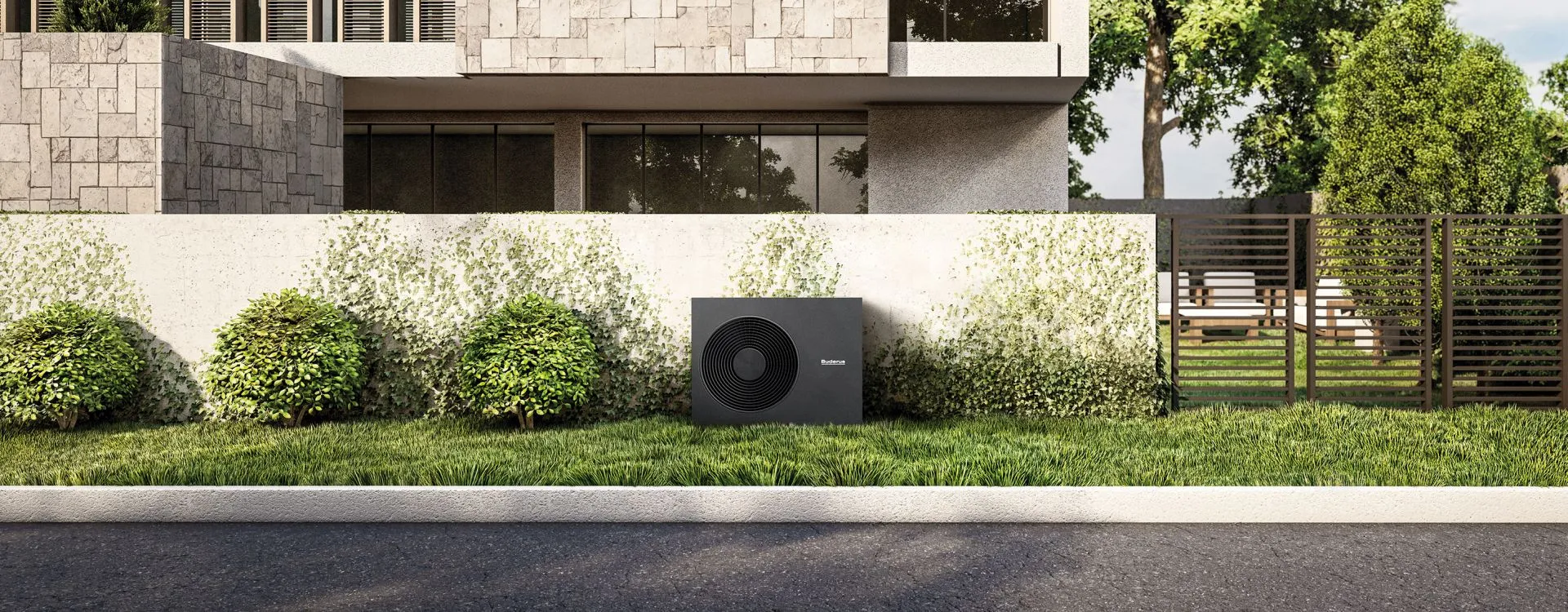Eine Wärmepumpe von Buderus steht auf einer grünen Wiese vor einer leicht bewachsenen Mauer eines modernen Hauses. 