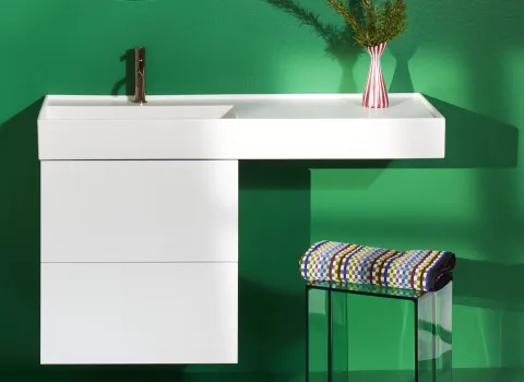 Ein moderner weißer Waschtisch mit erweiterter Ablagefläche steht vor einer kräftig grünen Wand.