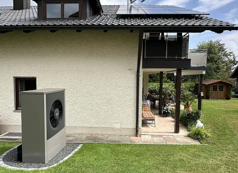 Seitliche Ansicht eines Einfamilienhauses mit Photovoltaikanlage und installierter Wärmepumpe im Gartenbereich.