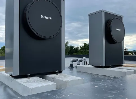 Zwei Wärmepumpen der Marke Buderus sind auf einem Betonsockel auf ein Flachdach montiert.