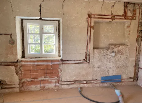 Eine Wandheizung mit sichtbaren Kupferrohren umrahmt das Fenster.