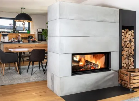 Ein großzügiger Wohn-Essbereich mit modernem Design zeigt einen großen, eckigen Kamin aus Beton mit loderndem Feuer. 