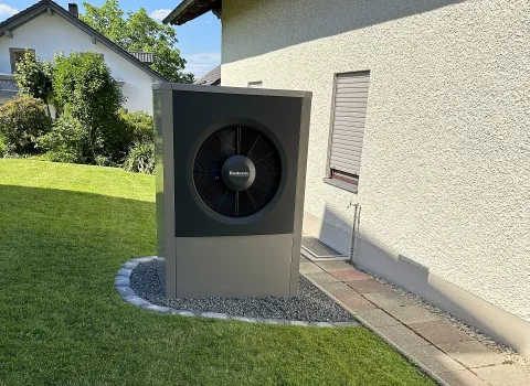 Eine Buderus-Wärmepumpe steht auf einem Kiesbett neben dem Haus.