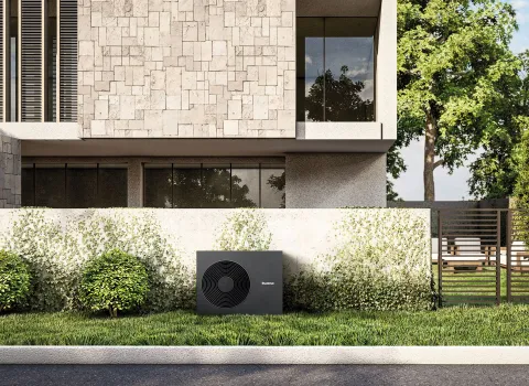 Eine Wärmepumpe von Buderus steht vor einem modernen Haus auf einen Grünstreifen.