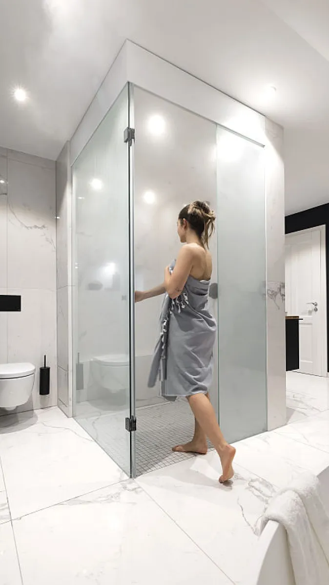 Eine Frau öffnet die Tür zur nebligen Dampfdusche.