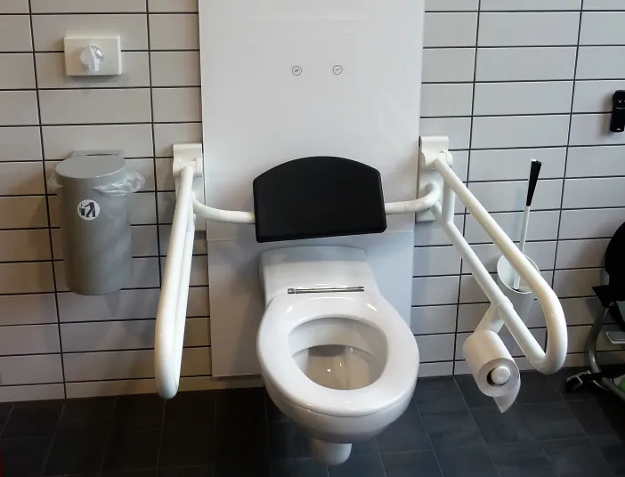 Barrierefreies WC mit Stützgriffen vor weißen Fliesen.