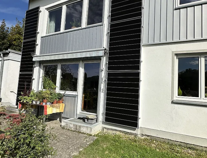 An der Fassade eines modernen Wohnhauses sind schmale, vertikale Photovoltaik-Module beidseitig neben den Fenstern installiert.