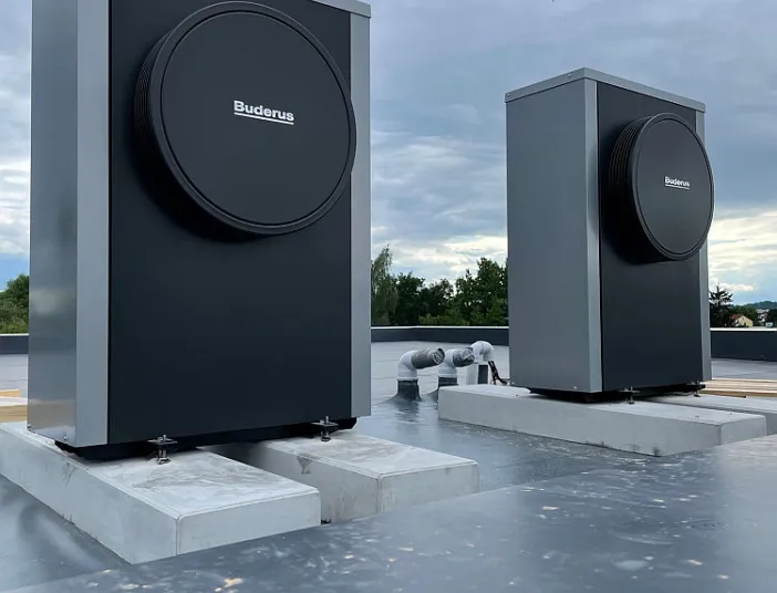 Zwei Wärmepumpen der Marke Buderus sind auf einem Betonsockel auf ein Flachdach montiert.