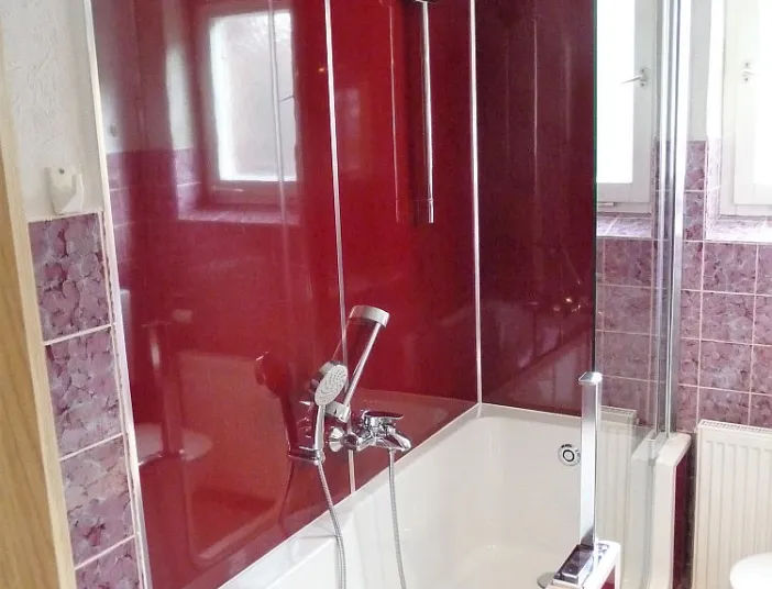 Ein modernes Badezimmer mit einer Badewanne, die von glänzenden, weinroten Wandpaneelen eingerahmt ist. 