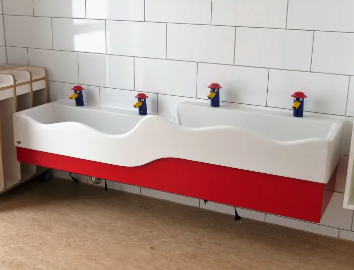 Ein doppeltes Waschbecken mit wellenförmigem Rand ist an einer gefliesten Wand montiert, ideal für den Einsatz in Kindergärten oder Kitas. 