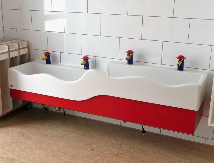 Ein doppeltes Waschbecken mit wellenförmigem Rand ist an einer gefliesten Wand montiert, ideal für den Einsatz in Kindergärten oder Kitas. 